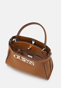 Sac à main synthétique marron avec une forme structurée, quincaillerie dorée et logo "GUESS" en relief. Présente une poche intérieure et une texture lisse.