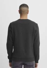 Sudadera negra de cuello redondo con mangas largas, que presenta un diseño sencillo y puños acanalados, vista desde la parte de atrás. Textura suave.