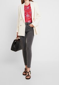 White blazer, red floral patterned top, gray skinny jeans, black handbag with tortoiseshell handles, and black strappy sandals.