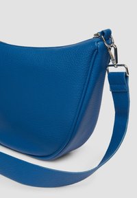 Blaue Leder-Schultertasche mit glatter Textur, geschwungener Form und verstellbarem Gurt. Reißverschluss und sichtbare Metallbeschläge.