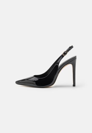 Czarny lakierowany but na wysokim obcasie typu slingback z szpiczastym noskiem i paskiem wokół kostki z złotą klamrą na białym tle.