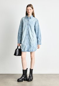Heled sinine teksakleidiga, millel on nööbistamine, pikad varrukad ja CK logo muster. Must käekott ja tublid mustad saapad täiustavad outfiti.