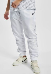 Weiße Sporthose mit schwarzen seitlichen Streifen, elastischen Bündchen und einem Logo. Das Material wirkt glatt und glänzend, geeignet für Sportbekleidung.