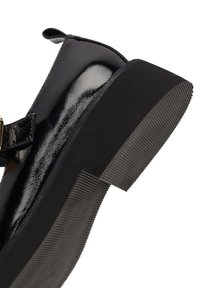 Schwarzer Lacklederschuh mit einer klobigen Gummisohle, runder Zehenpartie und einem Riemen mit einem metallischen Schnallen-Detail.