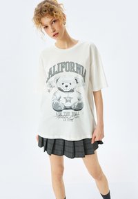 Hvid oversized t-shirt med et grafisk motiv af en teddy-bear, tekst "CALIFORNIA" og et stjernedesign. Blødt stof, rund halsudskæring, korte ærmer.