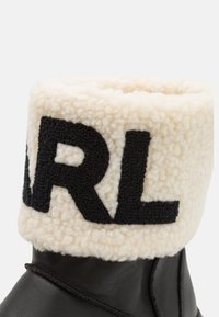 Botín de cuero negro con un puño de borlas color crema. Gran texto negro que dice "ARL" en el puño, mostrando un diseño de tejido texturizado.