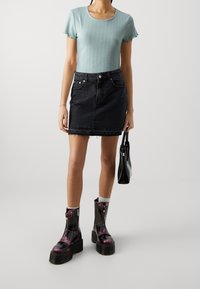 Ljusblå räfflad kortärmad topp, svart jeanskjol med fransad nederkant, kraftiga svarta och lila dragkedjeskor, och en liten svart handväska.