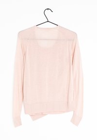 Rosa stickad tröja med avslappnad passform, ribbad nederkant och ärmslut, samt öppen ryggdesign. Hänger på en svart metallkrok.