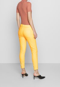 Gula smala jeans med en slät textur, dragkedjeaccent vid anklarna, parat med en kortärmad rosa ribbade topp och svarta mules.