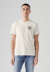 Tricou din bumbac crem cu mâneci scurte, având un design grafic negru cu textul "HOUSE PLANTS" și "Levi's" pe pieptul stâng.