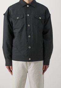 Svart rutig kavaj med en strukturerad design, två bröstfickor, stora silverknappar och en något kortad fåll.