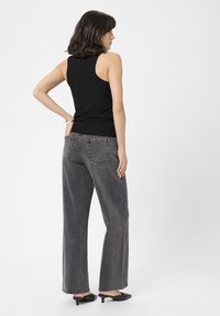 Sort ribbet tanktop iført med højtaljede, løstsiddende grå denimjeans og sorte hælede mules, set fra bagsiden.