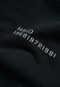 Svart tyg med vit tryckt text "HALO 196819721981". Texturen verkar mjuk och slät, med en minimalistisk design.