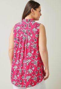 Top senza maniche di un brillante rosa con un motivo floreale nero. Presenta un collo alla coreana e pieghe sul retro per una maggior fluidità. Tessuto dalla texture liscia.