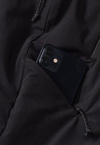 Black fabric pocket with a smartphone partially visible, featuring a smooth texture and two camera lenses. Drawstring closure detail visible.