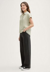 Camicia a maniche corte verde chiaro con bottoni e righe verticali, abbinata a pantaloni neri a vita alta e a gamba larga e sneakers nere.