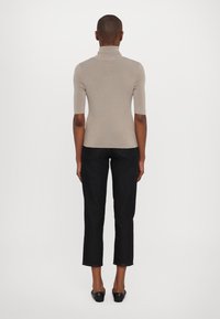 Suéter ajustado de cuello alto en color beige con mangas cortas, combinado con pantalones capri de mezclilla oscura, con dobladillo sin rematar y discretos bolsillos traseros.