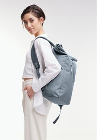 Gray fabric backpack with a roll-top closure and adjustable straps. Smooth texture with a side zip pocket and minimalist design.