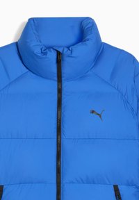 Blå polstret jakke med høj krave, sort lynlås foran og lille sort Puma-logo på venstre bryst.