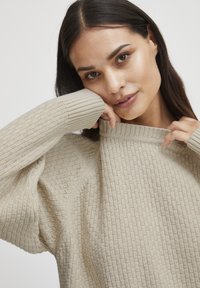 Pull en tricot texturé beige avec un col montant, des poignets côtelés et une coupe décontractée ; doté d'un motif géométrique et d'un tissu doux.