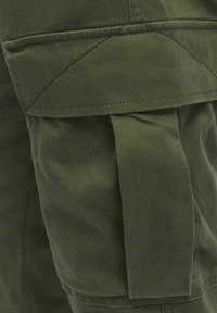 Nærbillede af en olivengrøn cargobuks lomme med klap og syninger.