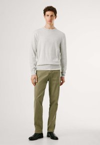 Suéter gris con cuello redondo, con dobladillo y mangas acanaladas, combinado con pantalones verde oliva. Botines negros de tobillo completan el conjunto.