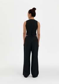 Black pinstripe crop top with a tie at the back, paired with wide-legged pinstripe trousers. Simple, fitted design with a textured finish.