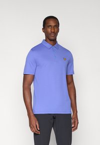 Kratka polo majica z raglani rokavi v svetlo vijolični barvi z ovratnikom, trojnim gumbom in rumenim logotipom na levi strani prsnega koša. Gladek tekstura.