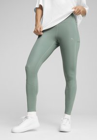 Strak zittende, hoog-waist legging van lichtgroene stof met matte afwerking. Kenmerken zijn onder andere contrasterende stiksels en een klein logo op de dij.