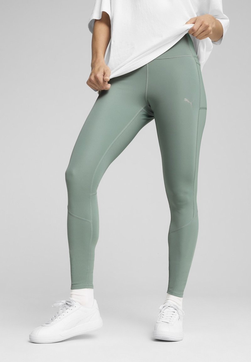 Strak zittende, hoog-waist legging van lichtgroene stof met matte afwerking. Kenmerken zijn onder andere contrasterende stiksels en een klein logo op de dij.