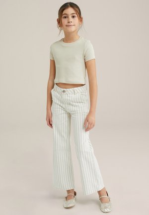 Jasno beżowy, prążkowany crop top z krótkim rękawem, w połączeniu z białymi spodniami w szerokie paski i błyszczącymi beżowymi butami.