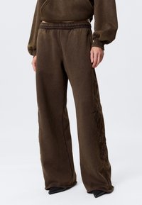 Bruine sweatpants met een elastische tailleband, wijde pijpen en getextureerde bloemenborduursels langs de zijkant. Gemaakt van zachte stof.