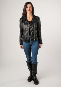 Zwarte leren motorjack met ritsdetails, gouden hardware en brede revers. Draagt met blauwe jeans en zwarte kniehoge laarzen.