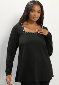 Top nero a maniche lunghe con scollatura quadrata, caratterizzato da bottoni decorativi bianchi lungo la scollatura e una vestibilità comoda. Tessuto liscio.