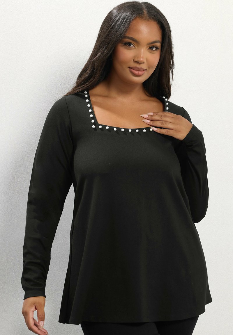 Top nero a maniche lunghe con scollatura quadrata, caratterizzato da bottoni decorativi bianchi lungo la scollatura e una vestibilità comoda. Tessuto liscio.
