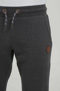 Pantalones de chándal grises hechos de una tela suave, con cintura elástica ajustable, parche de cuero marrón con el logo, y bolsillos laterales.