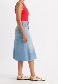 Röd, texturerad stickad linne kombinerad med en jeanskjol i A-linje med fransig fåll och vita sandaler med silverfärgade spänndetaljer.