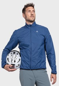 Blaues, leichtes Radtrikot mit hohem Kragen, Reißverschluss vorne und elastischem Saum. Das Modell hält einen weißen Fahrradhelm mit Lüftungsöffnungen.