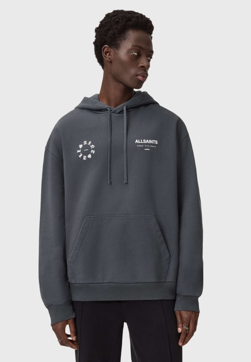 Ciemnoszara bluza z kapturem z miękkiego, teksturowanego materiału. Posiada przednią kieszeń oraz białe logowanie na klatce piersiowej. Kaptur z troczkami. Prosty, casualowy design.