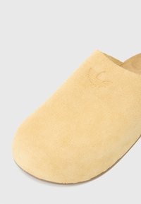 Yellow suede slip-on shoe with a rounded toe. Features embossed logo on the upper. Soft texture with a flat, light-colored sole.