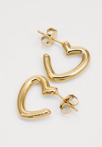 Orecchini a forma di cuore in oro con una finitura liscia e lucida. Presentano una chiusura a perno e un'incisione del marchio su un lato.