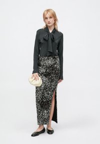 Naine kannab musta pika varrukaga pluusi koos lipsuga, musta ja hõbedase sädelevate täppidega seeliku, millel on külgsisene lõige, ja musti lapikese jalanõusid, hoides väidet beezist käekotti.