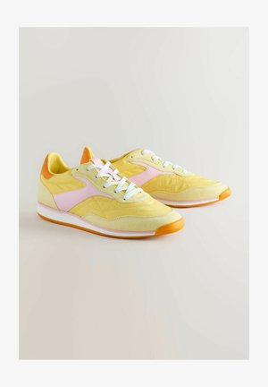 Rumene teniske s roza akcenti, oranžnim petam, belimi vezalkami in teksturiranimi plastmi; vsebuje klasičen atletski dizajn z gumijastim podplatom.