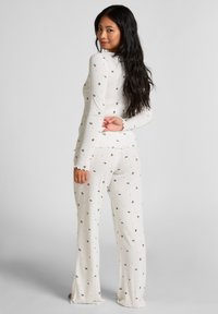 Conjunto de pijama de punto blanco que presenta pequeños patrones florales negros, con mangas largas y pantalones acampanados con bordes en forma de ola. Tejido suave y texturizado.