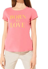 Lyserød bomulds t-shirt med korte ærmer og rund halsudskæring, der har teksten "BORN TO LOVE" i fed gule bogstaver på forsiden.