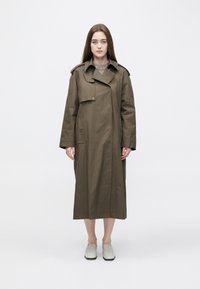Lång olivgrön trenchcoat med slagkrage, sidfickor och dubbelknäppt design. Slät, tålig tyg med avslappnad passform.
