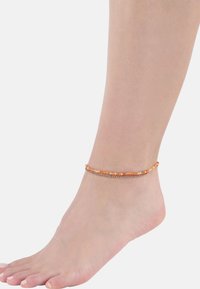 L'anklet di perline presenta perline arancioni e argento su una delicata catena, progettata per adattarsi attorno alla caviglia con una superficie liscia.