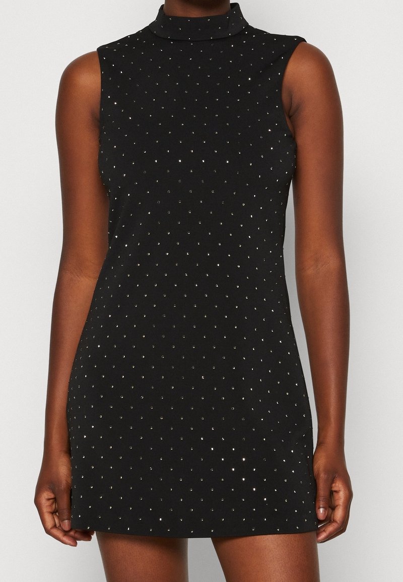 Robe courte noire sans manches avec col montant, décorée de petits clous argentés répartis de manière régulière.