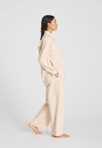 Beige pamut oversize ing és laza fitű széles lábú nadrág. Az ing hagyományos gallérral és gombos részletekkel rendelkezik.
