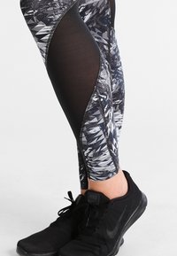 Black and gray leggings with a geometric pattern, made of stretchy material. Features black mesh panels and contrast stitching. Black athletic shoes.
